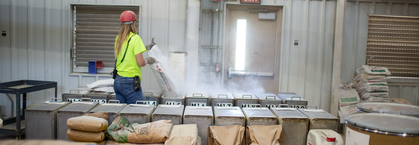 A staff member in a red hard hat fills containers at the feed mill.