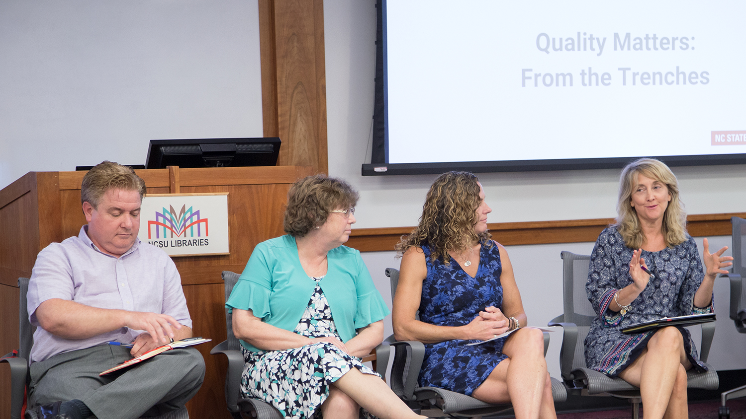 Four faculty members sitting lined up in discussion in front of a presentation and podium