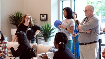 Director of Professional Development at the Career Development Center Marcy Bullock (center) speaks to participants at DELTA-Con in May. Bullock is holding a blue ball microphone and participants are actively looking at her. Photo in the CTI lobby.