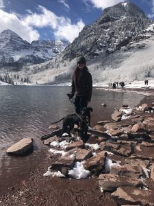 Monica and her dog, Abby, pictured by water and snowy mountains in Aspen, Colorado