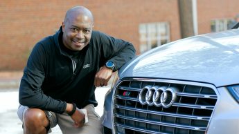Jeff Robinson posing with his car. He is kneeling down beside the front of his Mercedes.