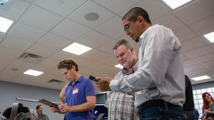 Mike Cuales shows a participant the GD 303 augmented reality application. Both people are looking down at a phone screen. 