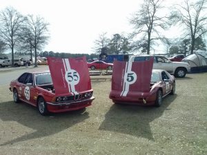 Two red and white, classic race cars with hoods open. 