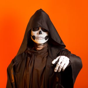 Arlene pictured in a black cloak and face paint in front of an orange background.