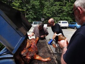 Howard and Cuales lean over a roast pig on a barbecue.