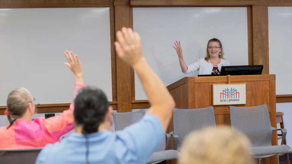 Associate Vice Provost for Academic Technology Innovation Donna Petherbridge welcomes faculty at the 2018 Summer Shorts in Instructional Technologies program. Petherbridge stands at front of room interacting with faculty. Faculty have hands raised.