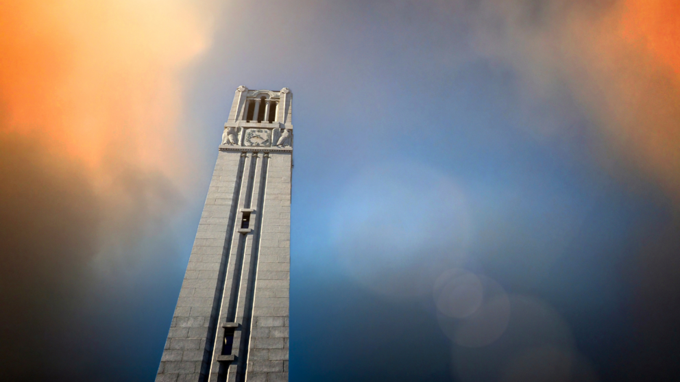 The NC State belltower against a blue and orange sky.