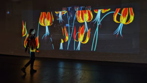 Hissam walks up to her artwork projected on a wall.