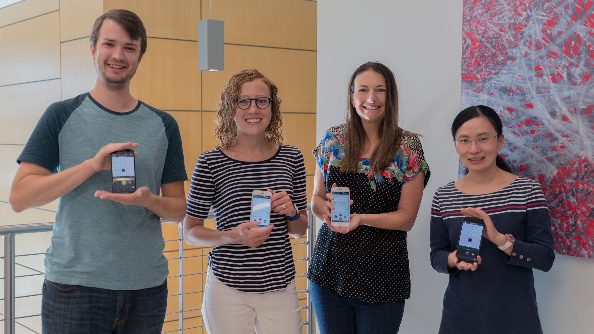 Four project members holding their phones and smiling in the CTI lobby.