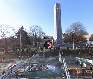 Runners begin the Krispy Kreme Challenge in front of the NC State Bell Tower on a sunny day. There is a donut icon in front of the image from the VR experience.