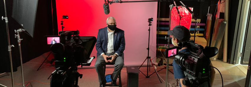 Chancellor Randy Woodson films a video for the Wicked Problems, Wolfpack Solutions course. He is pictured in front of a camera with producer Todd Buker instructing.