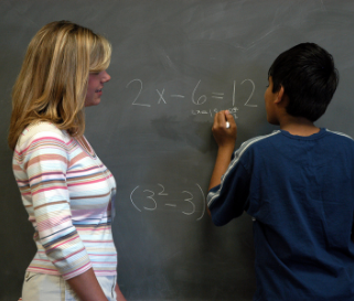 Teacher helps student work on math problem on a chalkboard.
